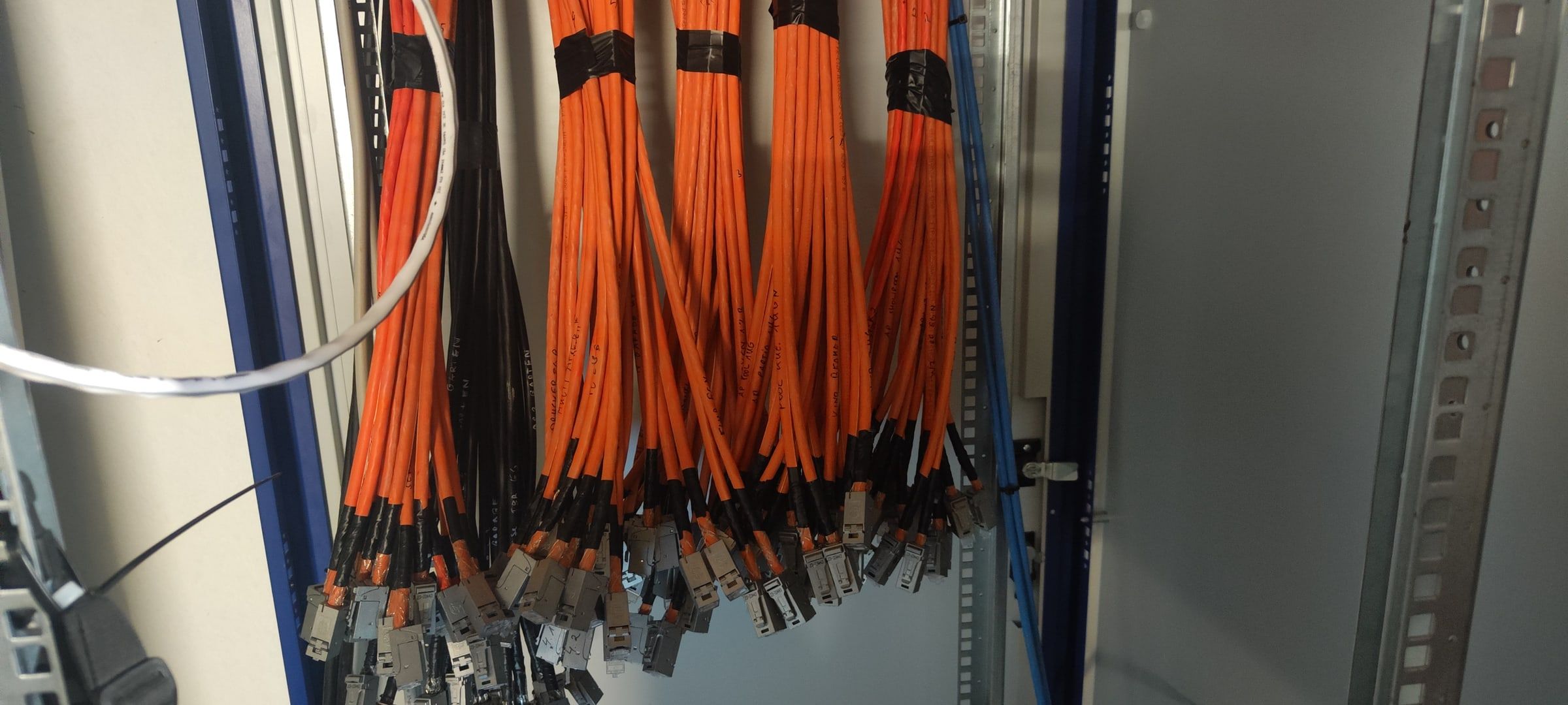 Gebündelte orangefarbene CAT-Kabel mit aufgelegten Steckern, jede Ader von Hand beschriftet.