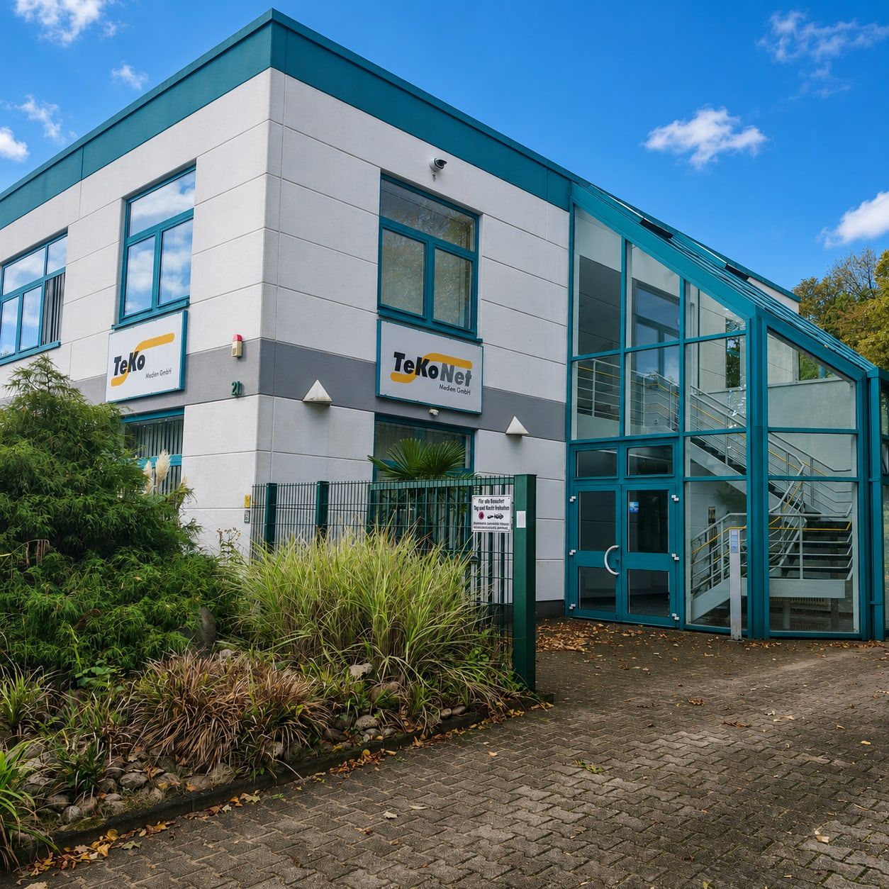 Firmengebäude der TeKoNet Medien GmbH in Essen mit Firmenschild an der Fassade und verglastem Treppenhaus.