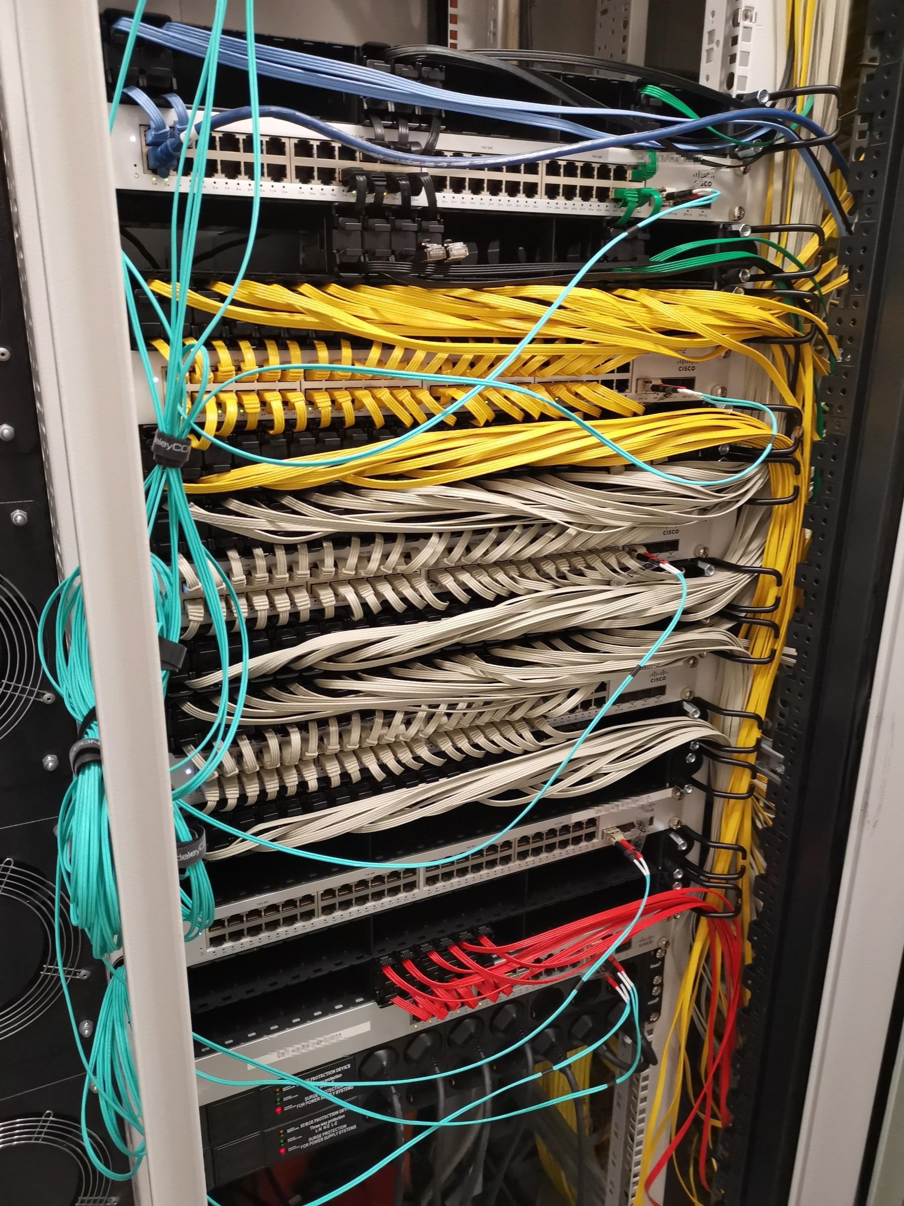 Netzwerkschrank mit sauber gebündelten Patchkabeln an mehreren Switches, farblich nach Verwendung getrennt.